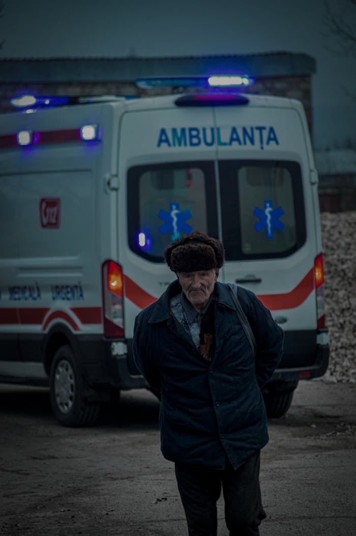 Elderly man walking in front of ambulance on city street during the evening.