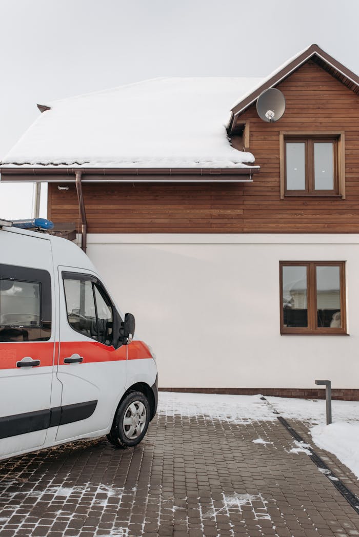 An ambulance parked beside a snowy house in a serene residential neighborhood.