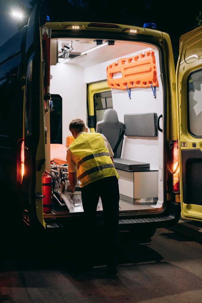 A paramedic wearing a reflective vest loads a gurney into an ambulance at night, highlighting emergency response.