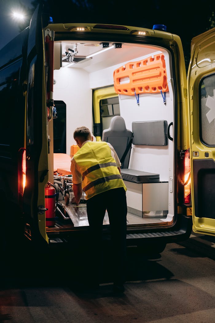 A paramedic wearing a reflective vest loads a gurney into an ambulance at night, highlighting emergency response.